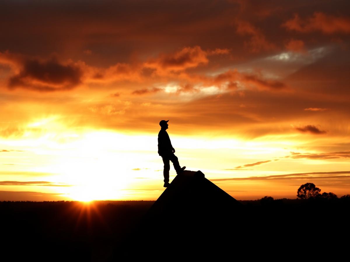 Roofer silhouetted on a roof ridge at sunset